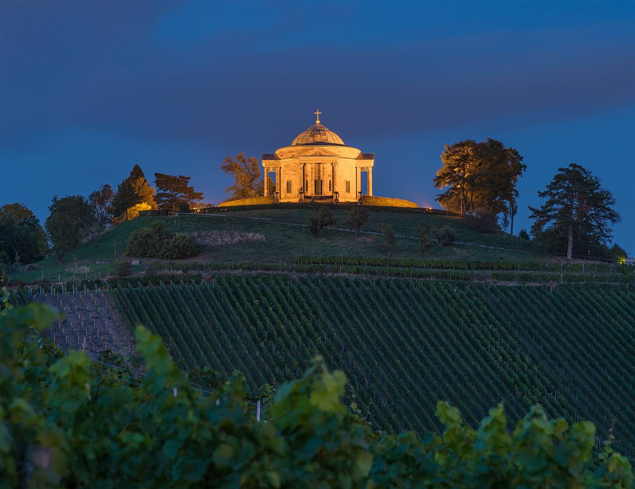 Die Grabkapelle auf dem Württemberg thront abends angestrahlt über den Weinbergen bei Stuttgart